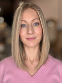 Woman with blonde hair and blue eyes wearing a pink sweater against a blurred background